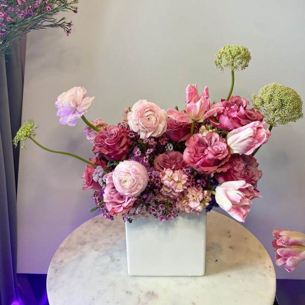 Pink and lavender floral arrangement in a white square vase