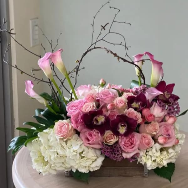 Pink and white floral arrangement with calla lilies, roses, and orchids in a box