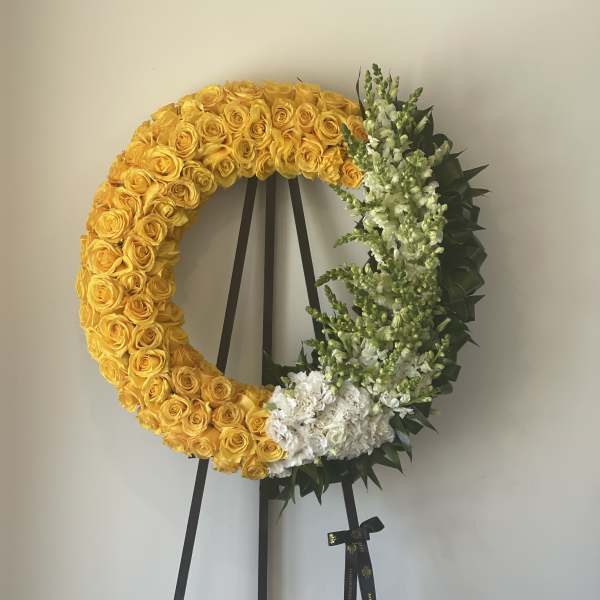 Yellow rose wreath on a black easel with white flowers and greenery