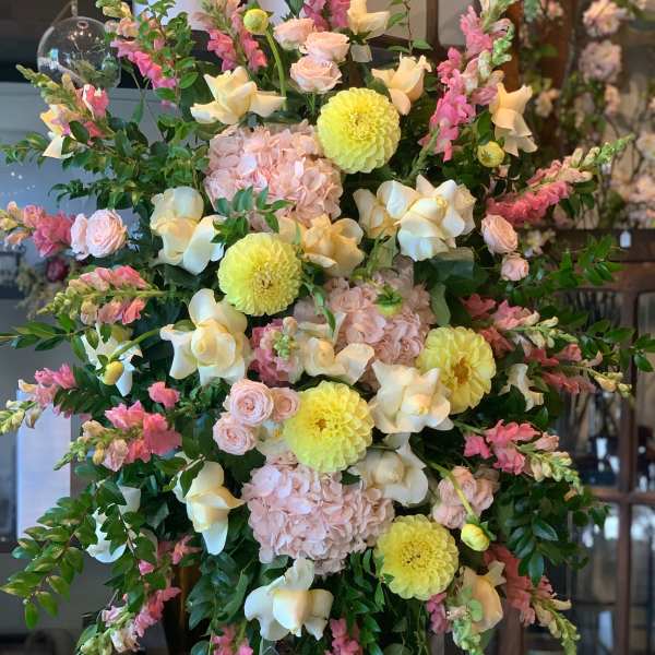 Large pastel floral arrangement on an easel with pink, yellow, and white blooms