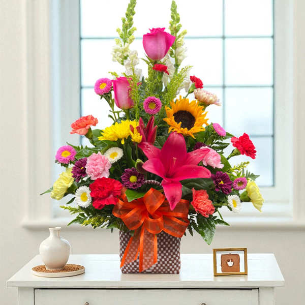 Tall mixed arrangement of bright flowers in a checkered box with an orange bow