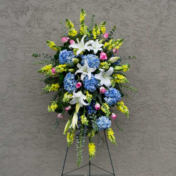Standing floral spray with white lilies, blue hydrangeas, and yellow snapdragons