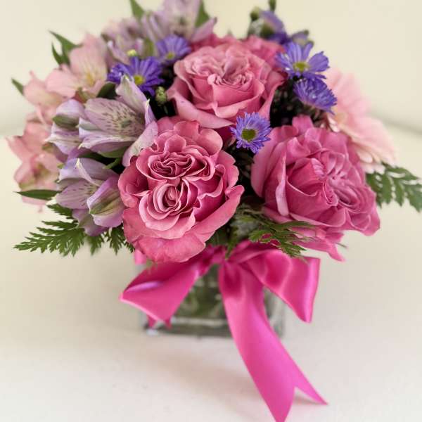 Pink roses and purple flowers in a glass vase with a bright pink ribbon