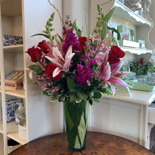 Tall bouquet of red roses and pink lilies in a green glass vase