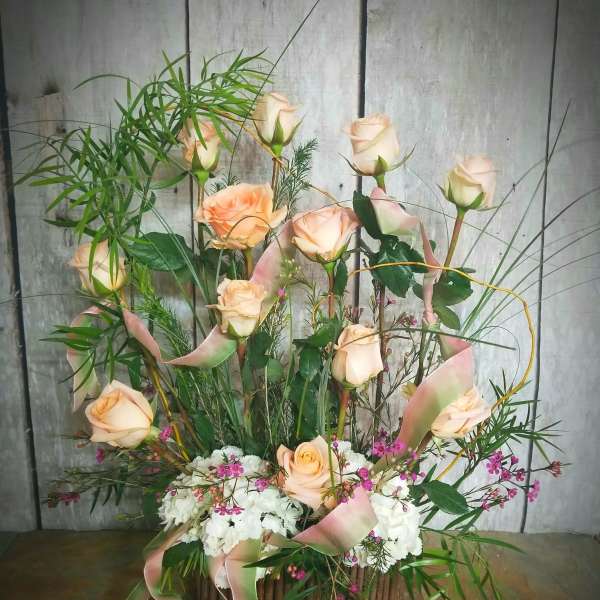 Tall arrangement of peach roses, white flowers, and pink ribbons