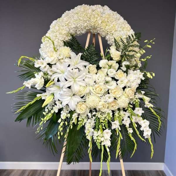 Large white funeral wreath on an easel with lilies and roses