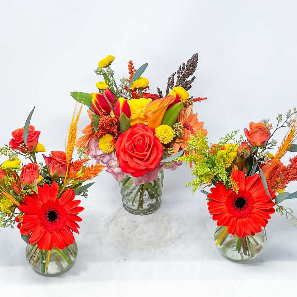 Three colorful floral arrangements in glass vases with red gerbera daisies and roses