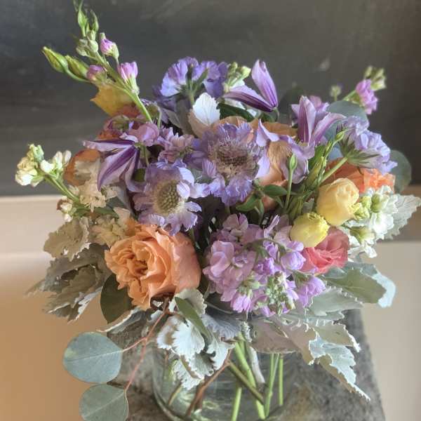 Pastel bouquet of peach, pink, and purple flowers in a glass vase