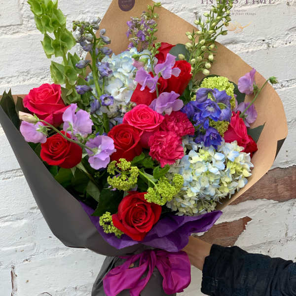 Bouquet of red roses, blue hydrangeas, and purple flowers wrapped in brown paper