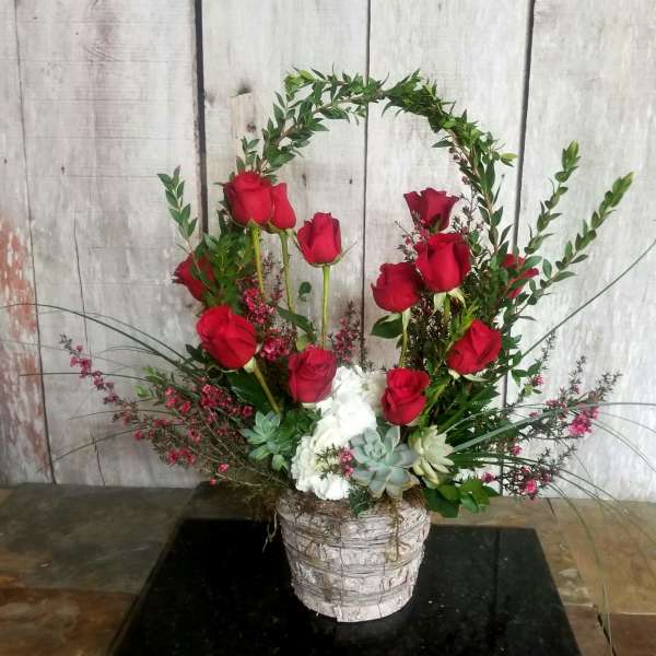 Red roses arranged in a white basket with succulents and greenery