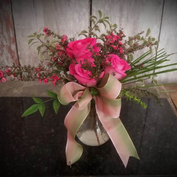 Pink roses in a clear vase with a large pale ribbon bow