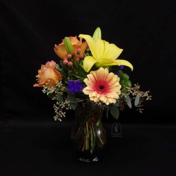 Mixed bouquet with yellow lily, peach roses, and a gerbera daisy in a glass vase