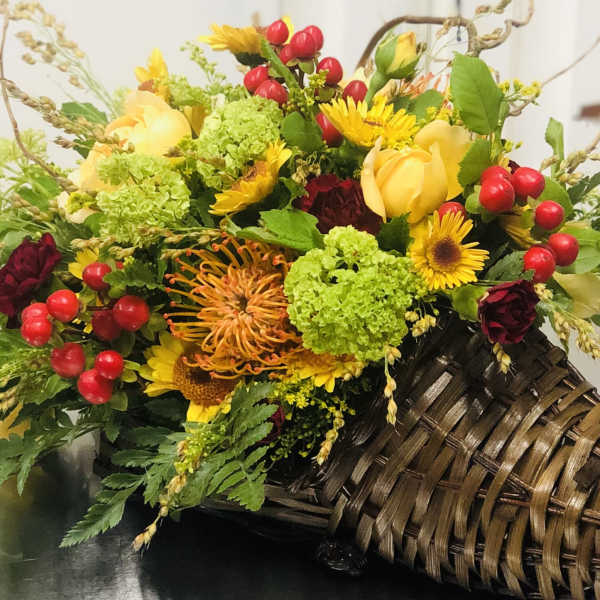 Mixed bouquet with yellow roses, red berries, and green blooms in a woven basket
