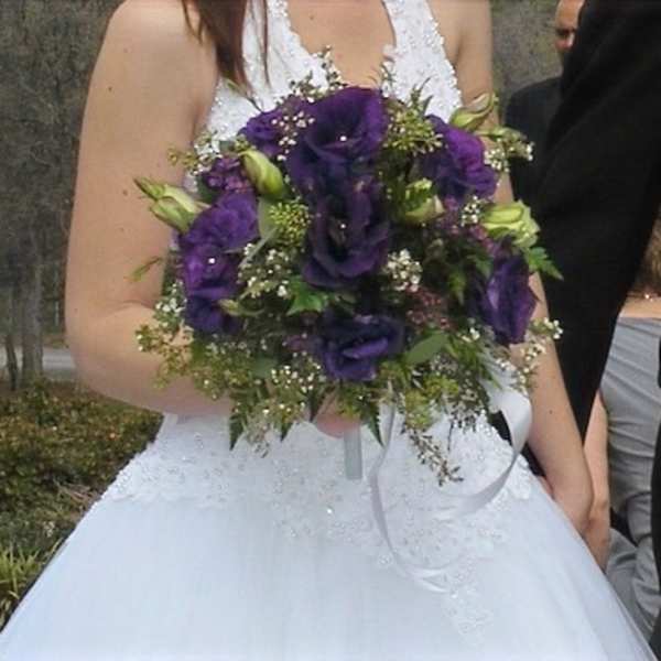 Bride holding a bouquet of purple flowers with white ribbon