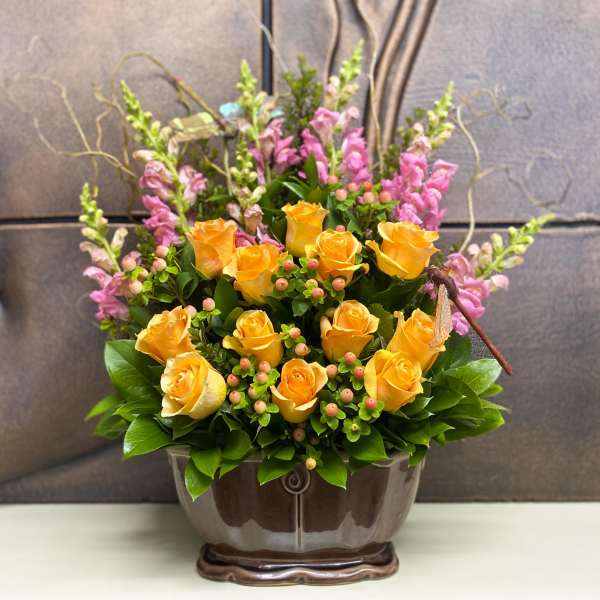 Yellow roses and pink snapdragons in a brown ceramic vase