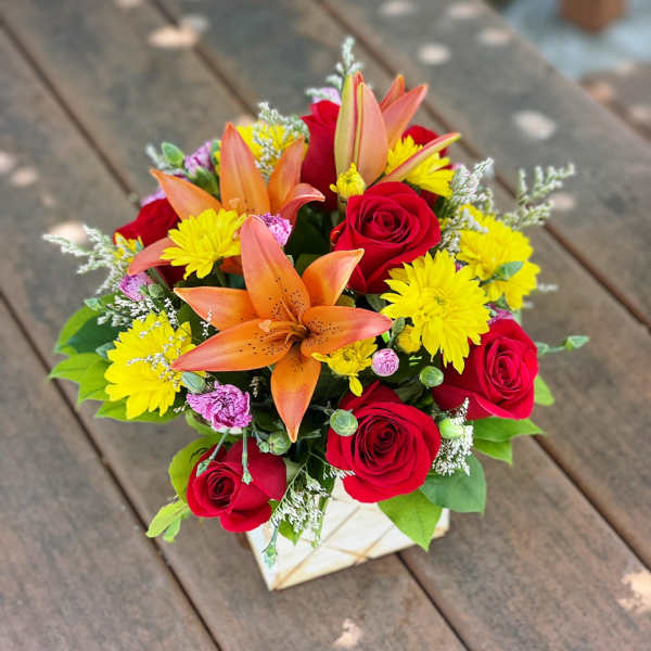 Bouquet of red roses, orange lilies, and yellow daisies in a square box