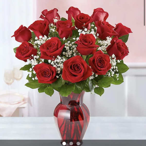 Red roses arranged in a red glass vase with white filler flowers