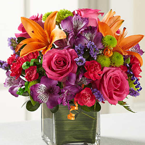 Pink and purple bouquet with orange lilies in a square glass vase