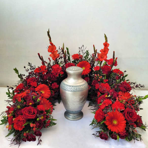 Red floral funeral arrangement surrounding a silver urn