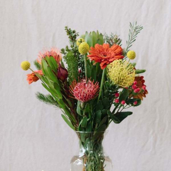 Mixed bouquet of orange and pink flowers in a clear glass vase beside a candle