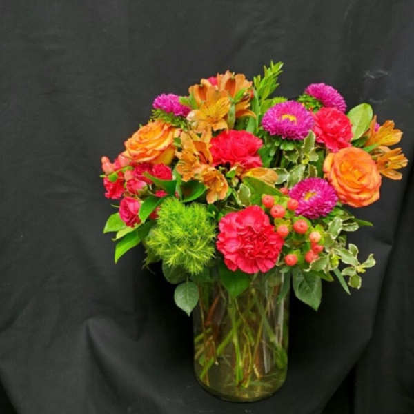 Mixed bouquet of orange, pink, and red flowers in a glass vase