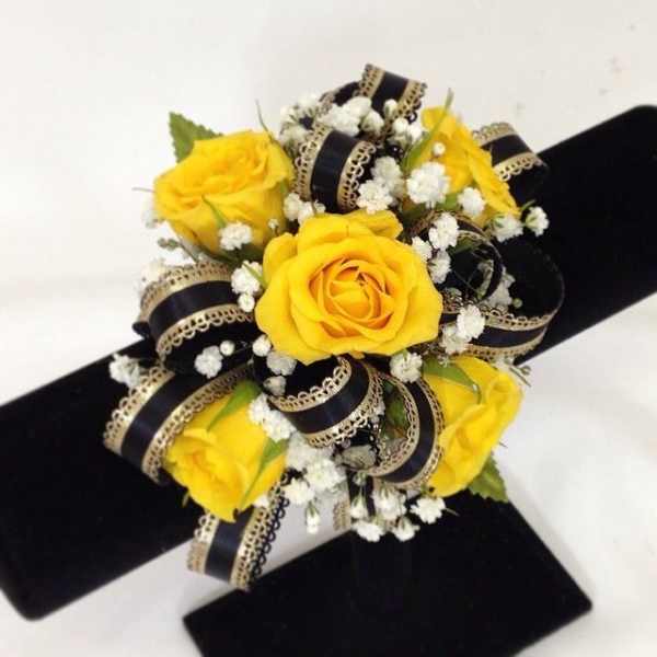 Yellow roses with white filler flowers and black ribbon on a wrist corsage