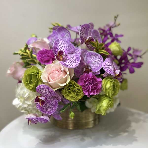 Purple orchids with pink roses and green carnations in a gold container
