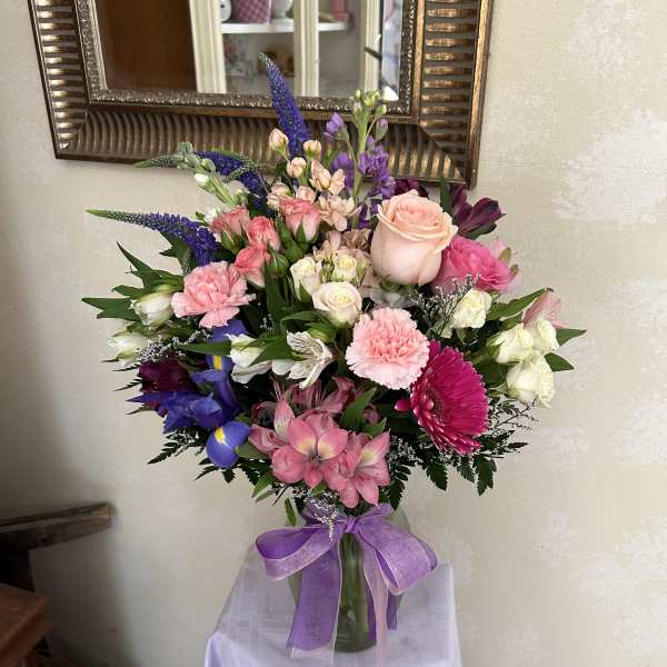 Mixed bouquet of pink, purple, and white flowers in a glass vase with a purple ribbon