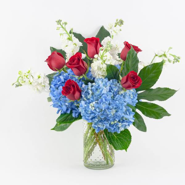 Red roses and blue hydrangeas in a clear glass vase