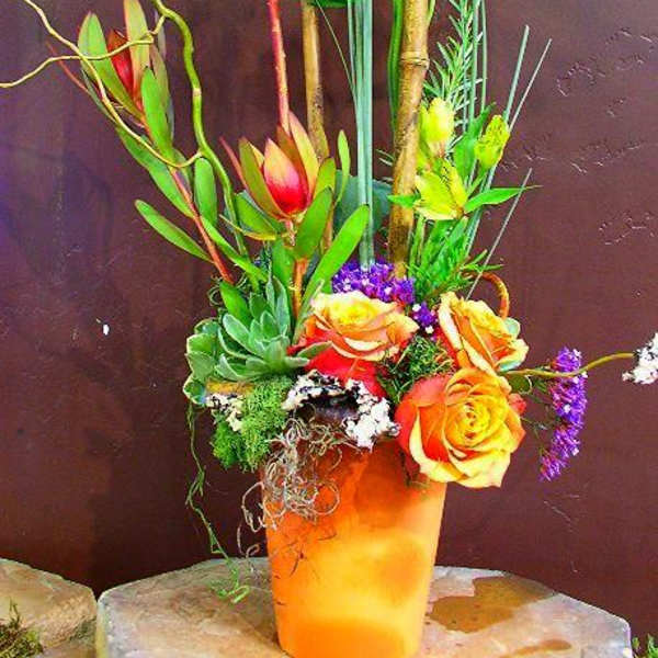 Tall tropical floral arrangement in an orange vase with orchids and roses