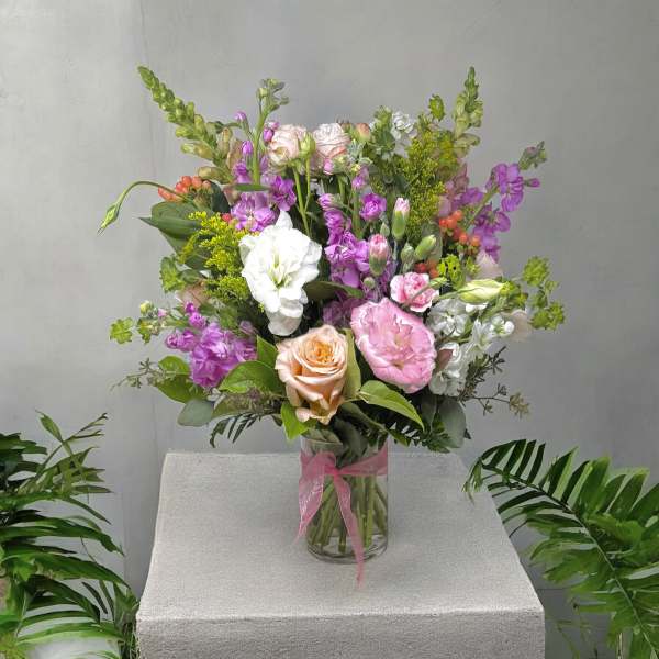 Mixed bouquet of pink, white, and peach flowers in a glass vase with a pink ribbon