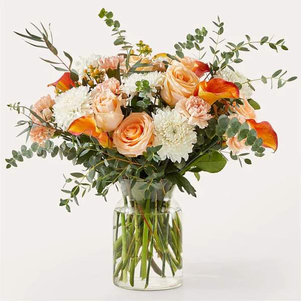 Bouquet of peach roses, white mums, and orange calla lilies in a glass vase