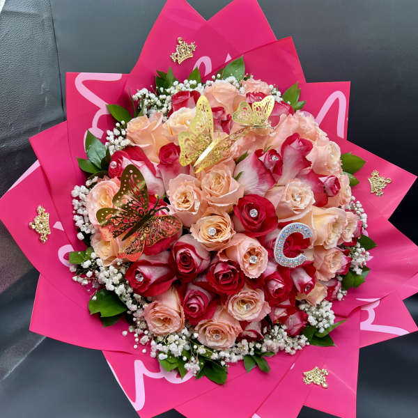 Round bouquet of red and peach roses wrapped in bright pink paper with gold butterfly accents.