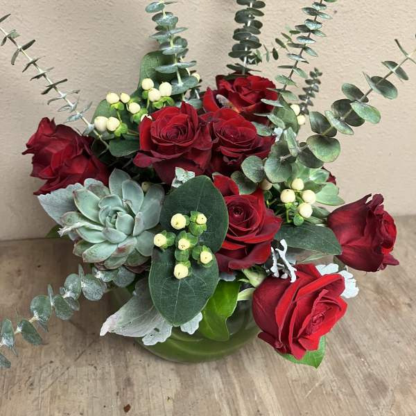 Red roses arranged with eucalyptus and a succulent in a green vase
