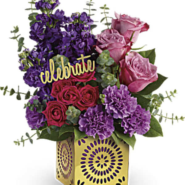 Purple and pink flower arrangement in a decorative gold vase with a "celebrate" sign