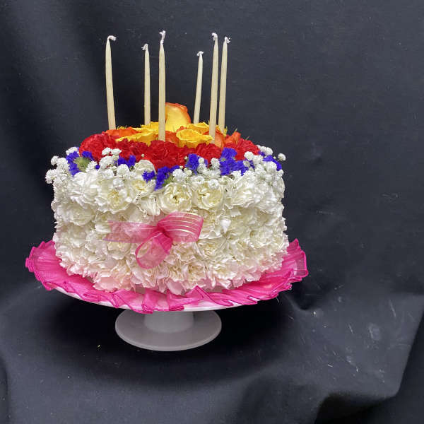 Round floral cake with white, red, yellow, and blue flowers and tall candles