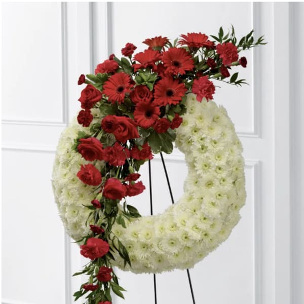 Red flowers cascade over a white floral wreath on a stand.