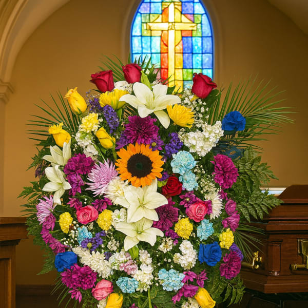 Large colorful funeral spray with roses, lilies, and a sunflower on an easel