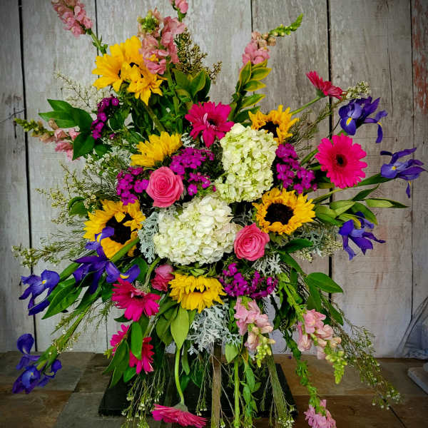 Large colorful standing floral spray with sunflowers, gerberas, roses, and irises