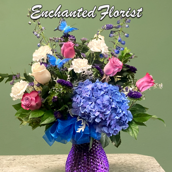 Mixed bouquet of blue hydrangea, pink roses, and white blooms in a purple glass vase