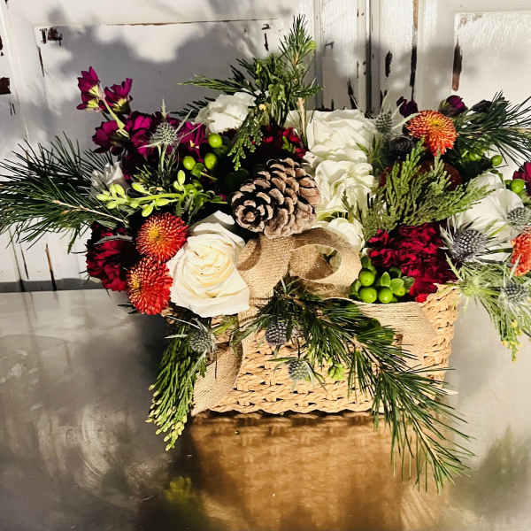 Holiday floral arrangement in a woven basket with pinecones and white roses