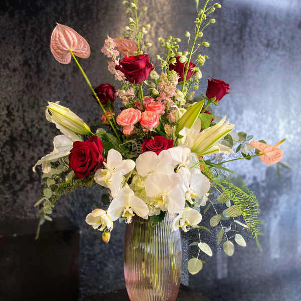 Mixed bouquet of red roses, white orchids, and lilies in a glass vase