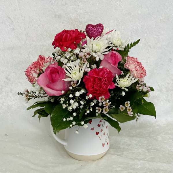 Pink and white mixed flower arrangement in a heart-decorated mug