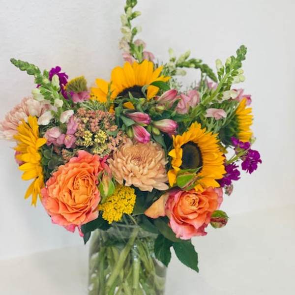 Mixed bouquet with sunflowers, peach roses, and pink blooms in a glass vase