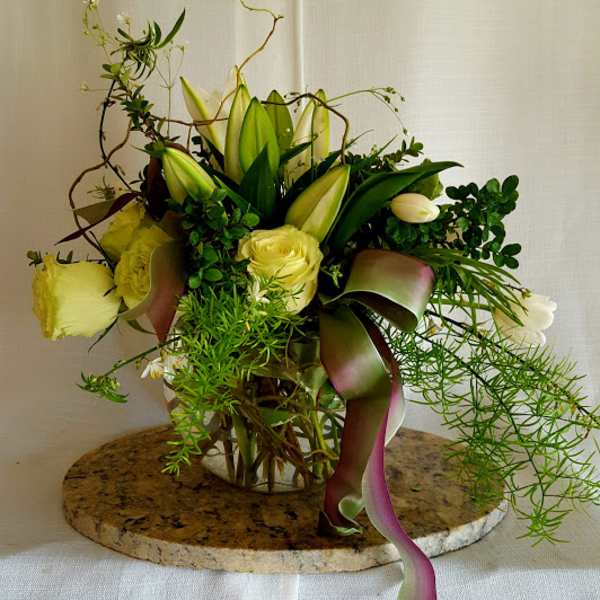 Yellow roses and lilies in a glass vase with trailing ribbon