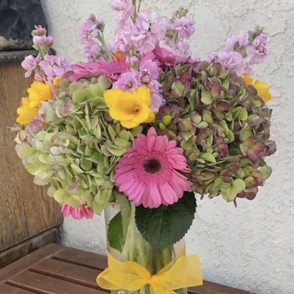 Pink and yellow mixed bouquet in a glass vase with a yellow ribbon