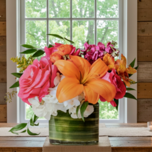 Bright mixed bouquet in a square glass vase with orange, pink, white, and purple blooms