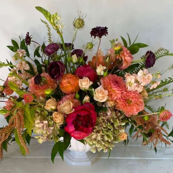 Large mixed bouquet in a white vase with pink, peach, and burgundy blooms