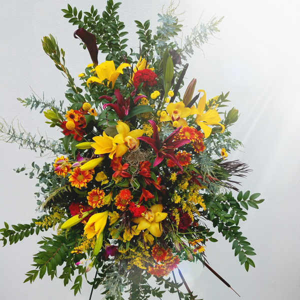 Large standing floral spray with yellow lilies and red-orange blooms