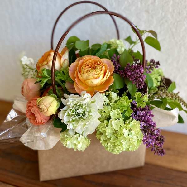 Peach roses, green hydrangeas, and purple flowers in a kraft box with curved handles